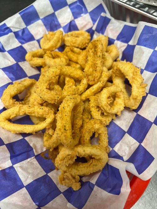 A plate of crispy, golden-brown fried calamari rings on a blue and white checkered paper.