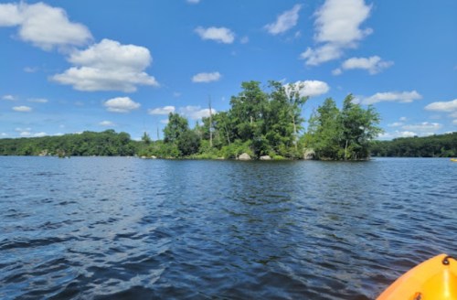 A serene lake scene with an island, surrounded by trees and blue skies dotted with fluffy clouds.