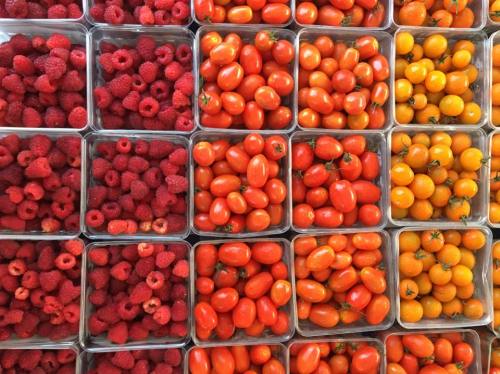 A colorful display of raspberries, orange cherry tomatoes, and yellow cherry tomatoes in clear containers.