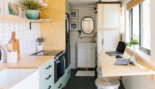 A modern tiny kitchen with a workspace, featuring light wood accents, plants, and a compact bathroom area.