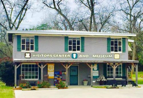 A two-story building with a sign reading "Visitors Center and Museum," surrounded by trees and a small garden.