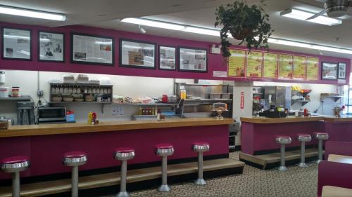 A colorful diner interior featuring a counter with stools, menu boards, and framed photos on the walls.