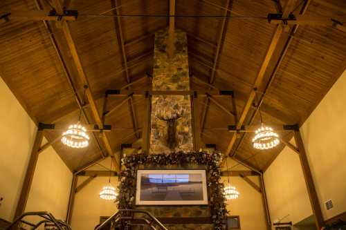 Interior of a rustic lodge with a high wooden ceiling, stone fireplace, and decorative lighting.