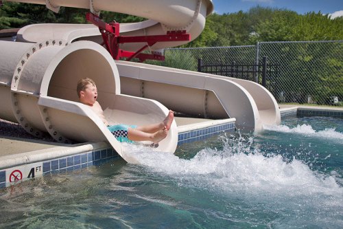 A child slides down a water slide into a pool, splashing water as they enjoy a sunny day at the water park.