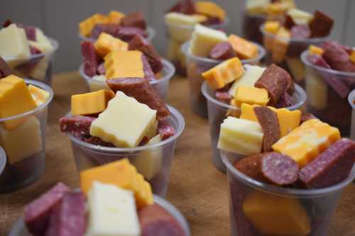 Cups filled with assorted cheese cubes and sliced meats arranged on a wooden surface.