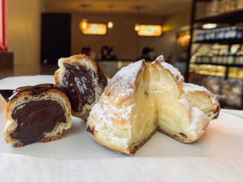Two pastries filled with chocolate and cream, dusted with powdered sugar, displayed on a white surface.