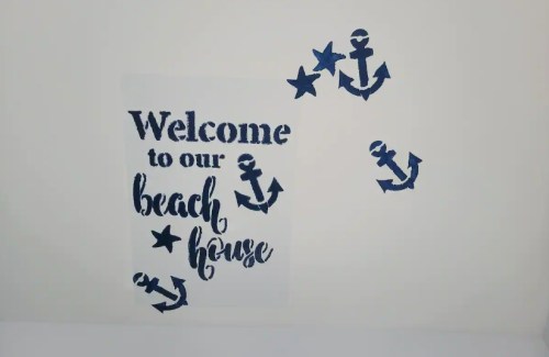 A wall decoration featuring the text "Welcome to our beach house" with navy blue anchors and stars.