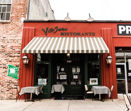 Exterior of Villa Jovan's Ristorante, featuring a striped awning, outdoor tables, and a red brick facade.
