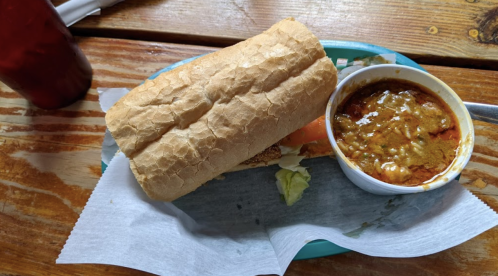 A sandwich on a plate next to a bowl of chili, served on a wooden table.