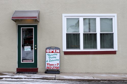 A storefront with a green door, open sign, and a window, displaying business hours for Thursday, Friday, and Saturday.