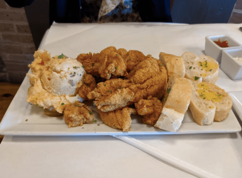 A plate of fried chicken, creamy mashed potatoes, and slices of bread with garlic butter.