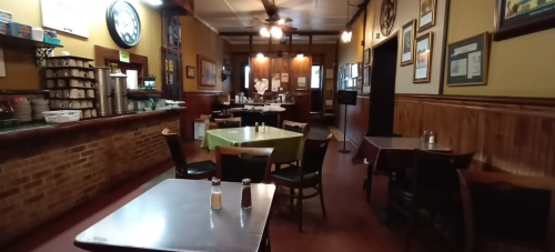A cozy restaurant interior with wooden walls, empty tables, and a counter in the background. Warm lighting creates a welcoming atmosphere.