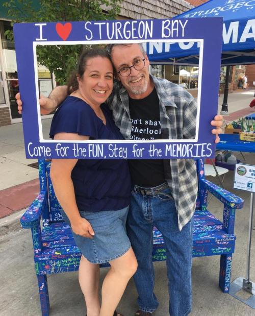 A man and woman pose together in a colorful frame that says "I ❤️ Sturgeon Bay" at a community event.