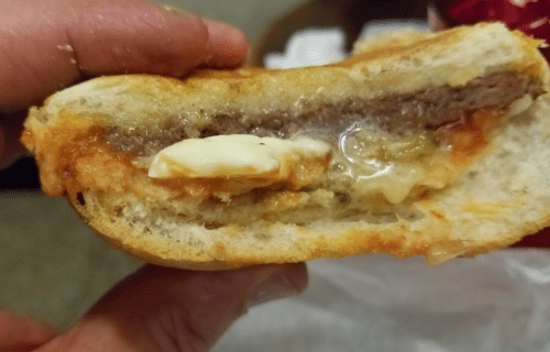 Close-up of a hand holding a cross-section of a sandwich with meat, sauce, and melted cheese inside.