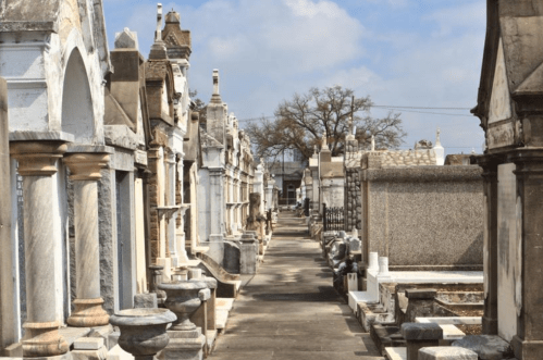 A serene cemetery pathway lined with ornate tombs and mausoleums under a blue sky.