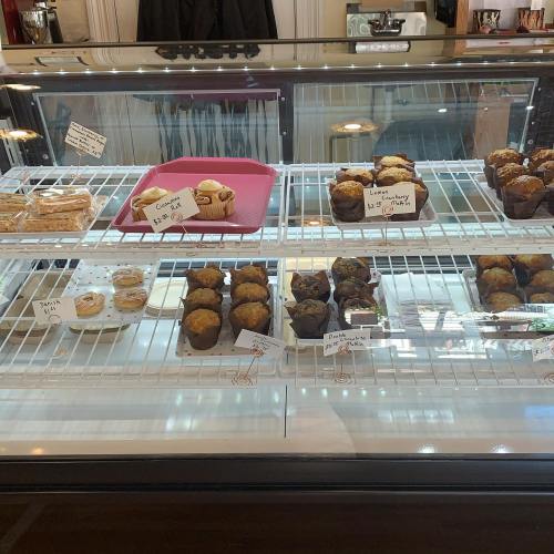 A display case filled with various baked goods, including muffins, cookies, and pastries, each labeled with prices.