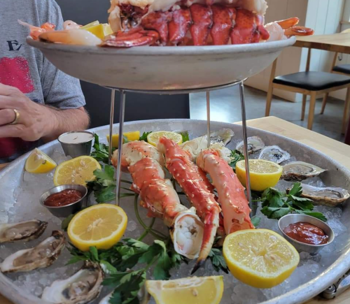 A seafood platter featuring lobster, crab legs, oysters, lemon wedges, and dipping sauces on a silver tray.