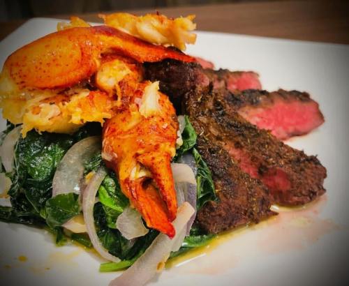 A plate featuring grilled steak, sautéed spinach with onions, and a lobster claw on top.
