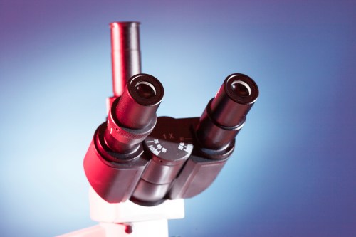 Close-up of a microscope eyepiece with dual lenses against a gradient blue background.