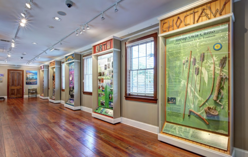 Interior view of a museum exhibit featuring informational displays on various topics, with wooden flooring and bright lighting.