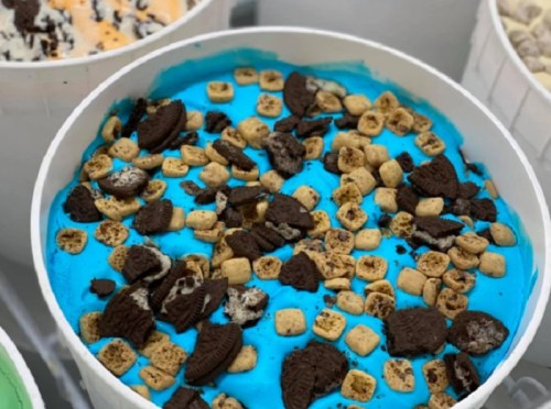 A round container filled with bright blue ice cream topped with crushed cookies and cereal pieces.