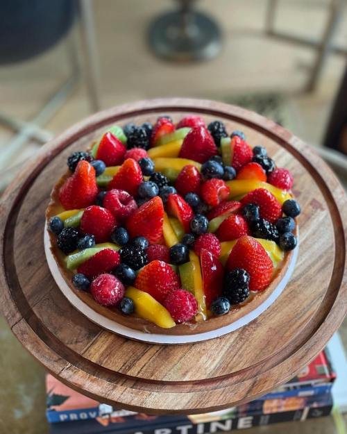 A colorful fruit tart topped with strawberries, blueberries, blackberries, and kiwi on a wooden serving board.