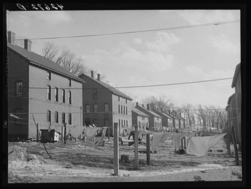 Row of brick buildings with clotheslines and laundry hanging outside, set against a cloudy sky.