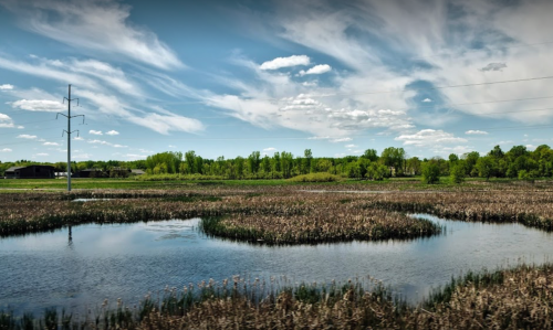 A serene landscape featuring a winding waterway, lush greenery, and a blue sky with scattered clouds.