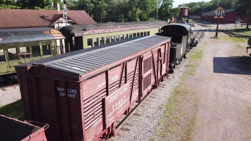 Aerial view of vintage train cars on a railway track, surrounded by greenery and historic buildings.