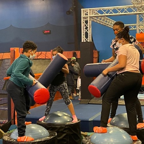 Children playing on a trampoline and foam obstacle course, wearing masks and engaging in active play.