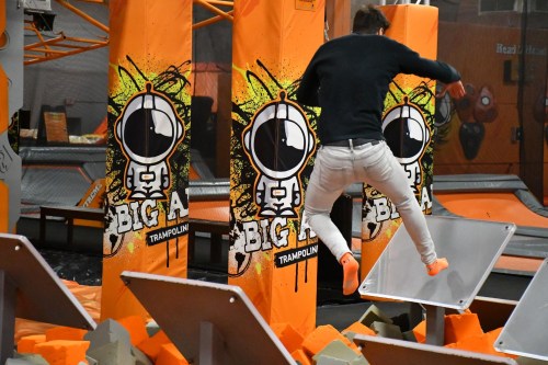 A person jumps between colorful trampoline pillars in a trampoline park, surrounded by foam blocks.