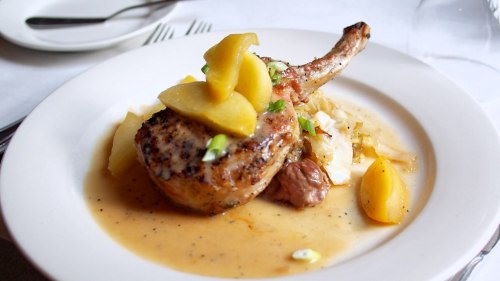 A plated pork chop topped with sliced apples, served on a bed of mashed potatoes with a savory sauce.
