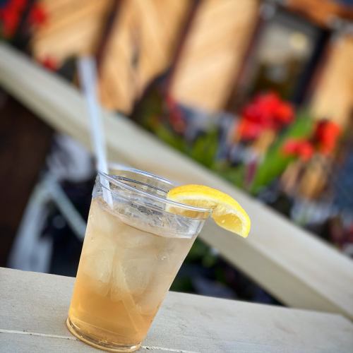 A refreshing drink with ice and a lemon slice, placed on a table with colorful flowers in the background.