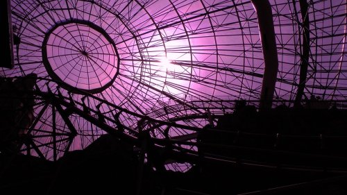 Abstract view of a geometric structure with a purple hue, featuring a circular opening and intricate metal framework.