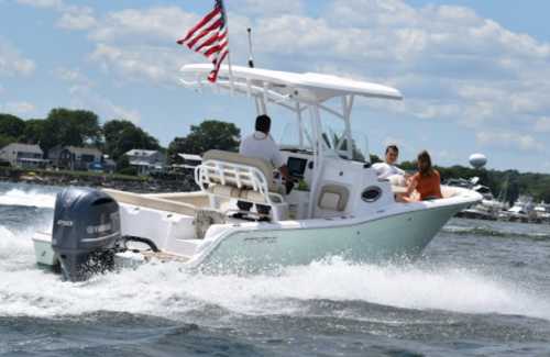 A boat with an American flag speeds through water, carrying three people on a sunny day.