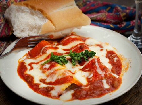 A plate of cheesy pasta with marinara sauce, garnished with parsley, alongside a piece of bread.