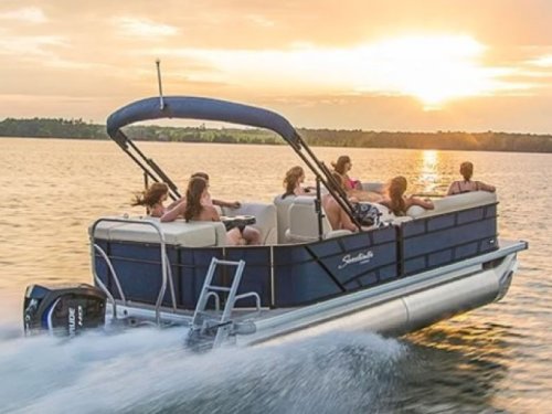 A group of people enjoying a sunset cruise on a pontoon boat on a calm lake.