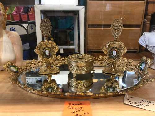 A decorative gold tray with two ornate candle holders and a small box, displayed on a mirrored surface.