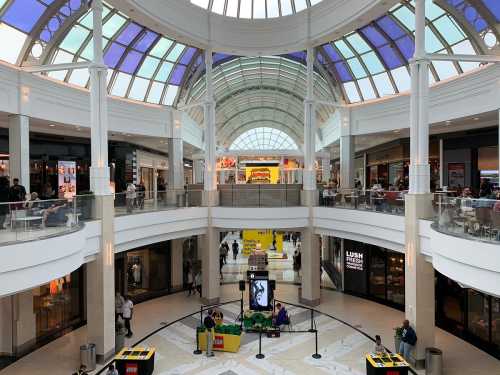 A spacious mall interior with a glass ceiling, shops on multiple levels, and a central display area.