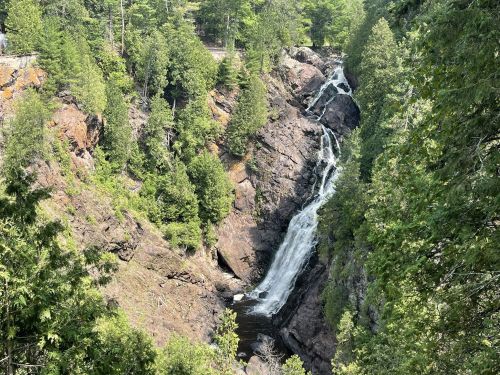 A scenic view of a waterfall cascading down rocky cliffs, surrounded by lush green trees.