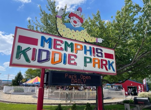 Colorful sign for Memphis Kiddie Park featuring a clown, with "Park Open" displayed below. Bright, cheerful atmosphere.