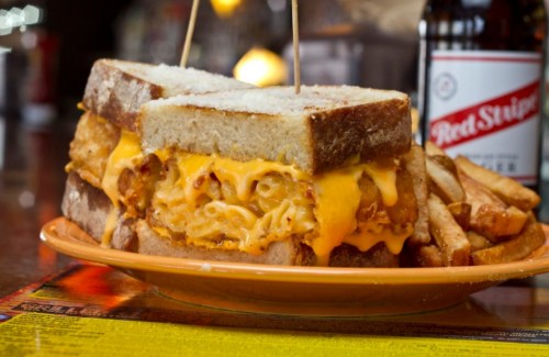 A hearty sandwich with fried chicken and macaroni and cheese, served with golden fries on the side.