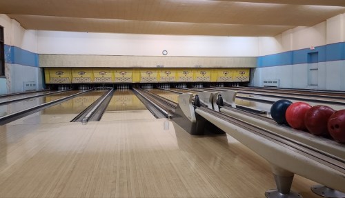 A bowling alley with empty lanes, colorful bowling balls on the side, and a clock on the wall.