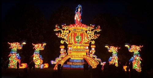 Colorful illuminated lantern display featuring a figure atop a decorative structure, surrounded by dragon sculptures at night.