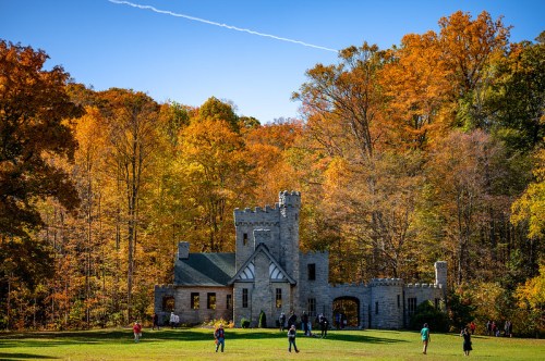 A stone castle surrounded by vibrant autumn trees and people enjoying the outdoors on a sunny day.