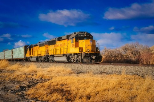 Two yellow Union Pacific locomotives pull a freight train along a track under a blue sky with scattered clouds.