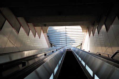 A view looking up an escalator with a modern, geometric ceiling and bright light at the top.