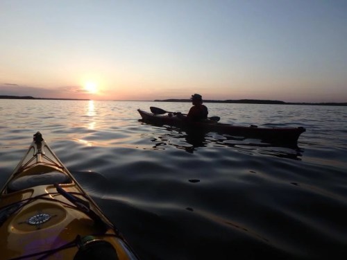 A serene sunset over a calm lake, with two kayakers enjoying the peaceful water.