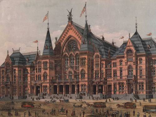 Historic building with ornate architecture, featuring towers, flags, and bustling street activity in front.