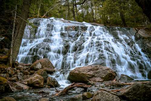 A serene waterfall cascading over rocky terrain, surrounded by lush greenery and large boulders.